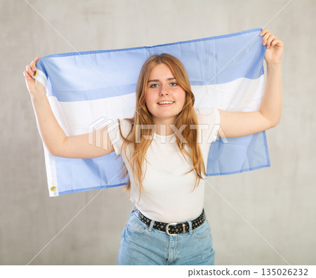 smiling girl in arms raised above head holds canvas of national flag of Argentina 135026232