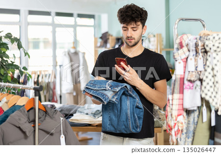Young shopper scanning jeans tag in outlet store Young shopper scanning jeans tag in outlet store 135026447