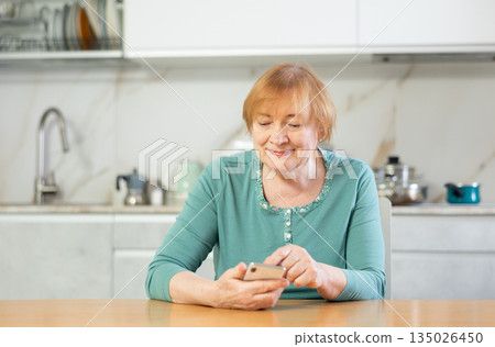 Adult woman reading message on phone in kitchen 135026450
