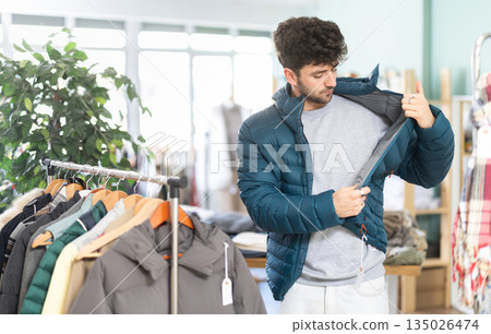 Young man trying on down jacket in clothing store Young man trying on down jacket in clothing store 135026474