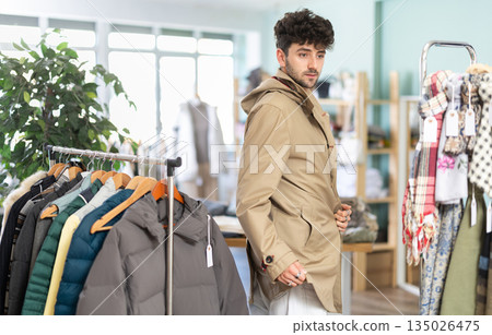 Young man tries on raincoat in clothing store Young man tries on raincoat in clothing store 135026475