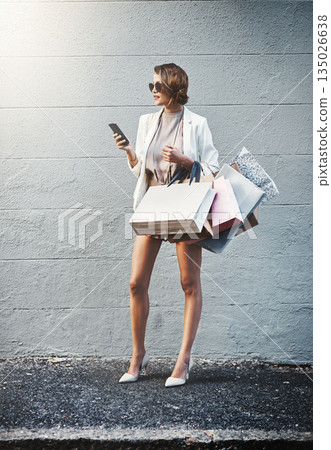 Shopping, outdoor and woman with a smartphone, retail and connection against a wall background. Female person, shopper or customer with bags, cellphone or boutique items with luxury, sale or discount Shopping, outdoor and woman with a smartphone, retail and connection against a wall background. Female person, shopper or customer with bags, cellphone or boutique items with luxury, sale or discount 135026638