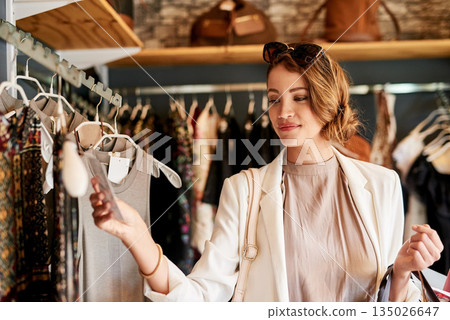 Retail, fashion and woman in a boutique, shopping and check price with discount, sale and clothes selection. Female person, customer or client buying outfit, choice and decision for items or products Retail, fashion and woman in a boutique, shopping and check price with discount, sale and clothes selection. Female person, customer or client buying outfit, choice and decision for items or products 135026647