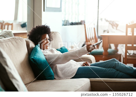 Black woman, watching tv and relax on couch with remote, home and happiness for me time, comedy or show. African girl, television and happy for movie, video or search on living room sofa in apartment Black woman, watching tv and relax on couch with remote, home and happiness for me time, comedy or show. African girl, television and happy for movie, video or search on living room sofa in apartment 135026712