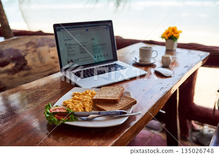 Cafe food, laptop or breakfast by a beach for remote workspace in the morning with connection. Desk, seaside restaurant or table in coffee shop for digital blog online with brunch meal or lunch Cafe food, laptop or breakfast by a beach for remote workspace in the morning with connection. Desk, seaside restaurant or table in coffee shop for digital blog online with brunch meal or lunch 135026748