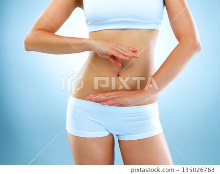 Woman, stomach and body with blue background with hands for diet and exercise for health. Model, fitness and women in studio for digestion diet and workout with weight loss for healthy living. Woman, stomach and body with blue background with hands for diet and exercise for health. Model, fitness and women in studio for digestion diet and workout with weight loss for healthy living. 135026763