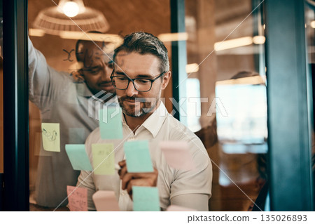 Businessman, writing and schedule planning in meeting for strategy, brainstorming or tasks at office. Man employee in leadership, presentation or training staff in team project plan at the workplace Businessman, writing and schedule planning in meeting for strategy, brainstorming or tasks at office. Man employee in leadership, presentation or training staff in team project plan at the workplace 135026893