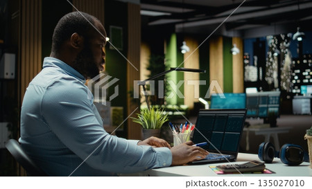 Black consultant reviewing data insights and managing agenda on laptop, drafting reports and proofreading to solve tasks. Notetaking supports goal setting for the business company. Black consultant reviewing data insights and managing agenda on laptop, drafting reports and proofreading to solve tasks. Notetaking supports goal setting for the business company. 135027010