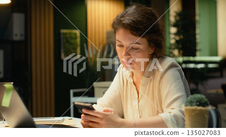 Confused employee checking her calendar before scheduling an engagement, picking up her mobile phone to answer texts and read notifications. Woman getting distracted and frowning. Camera B. 135027083