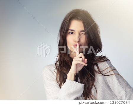 Woman, studio portrait and secret with finger on mouth for beauty deal, wink eye or icon for silence by background. Isolated model girl, cosmetics flirt or hand sign with emoji, whisper and makeup 135027084