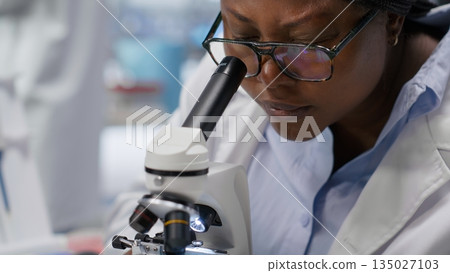 Microscope close up of woman arranging sample tray for experiment in chemistry lab. Detailed investigation of specimen for medical research and nanotechnology, biotechnology solutions. 135027103