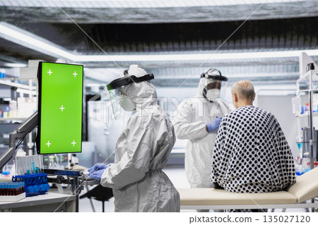 Vertical chroma key screen next to scientist in a biohazard facility treats a patient with infectious disease symptoms, study contamination control and vaccination methods for protection. Vertical chroma key screen next to scientist in a biohazard facility treats a patient with infectious disease symptoms, study contamination control and vaccination methods for protection. 135027120