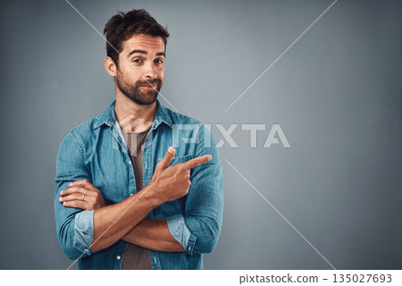 Portrait, pointing and man with mockup, promotion and opportunity against a grey studio background. Face, male person and model with casual outfit, decision and choice with happiness and showing 135027693