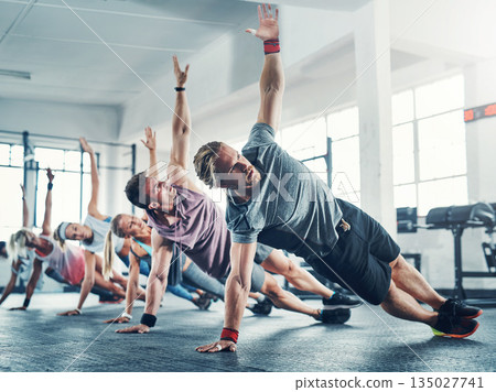 Fitness class, group training and friends doing a workout in the gym for health, wellness and flexibility. Sports, people and athletes doing a side plank exercise challenge together in sport studio. 135027741