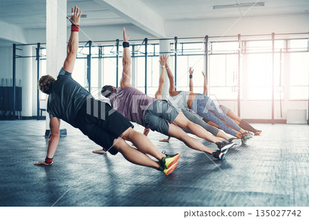 Fitness, group class and athletes doing a exercise in the gym for health, wellness and flexibility. Sports, training and people doing side plank exercise challenge together in sport studio or center. 135027742