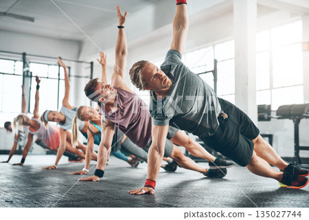 Gym class, group and athletes doing a workout for fitness, health or wellness flexibility. Sports, community and people doing a side plank exercise, training or challenge together in a sport studio. Gym class, group and athletes doing a workout for fitness, health or wellness flexibility. Sports, community and people doing a side plank exercise, training or challenge together in a sport studio. 135027744