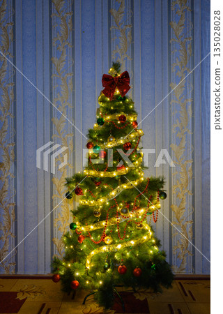 decorated christmas tree with a golden ribbon and a red bow by the wall 135028028