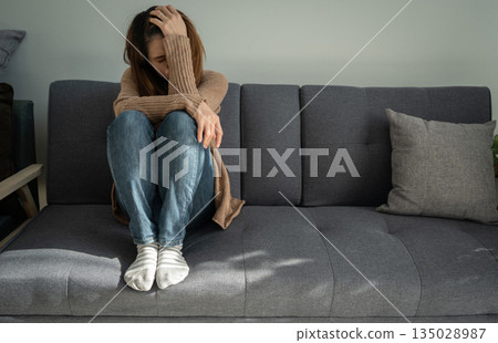 Depressed woman sitting alone in living room caused of sadness or broken heart. Depression is a form of highly negative thinking towards oneself, others and life. Depressed woman sitting alone in living room caused of sadness or broken heart. Depression is a form of highly negative thinking towards oneself, others and life. 135028987