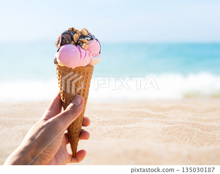 Hand Woman Holding Ice Cream Cone Scoop Choclota Taste Chocolate Strawberry on Sea Sand Beach at Coast Ocean Island, Tasty for Tourism Vacation Travel Summer Tropical Holidays. 135030187