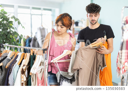 Young girl and guy browsing clothing racks in outlet 135030383