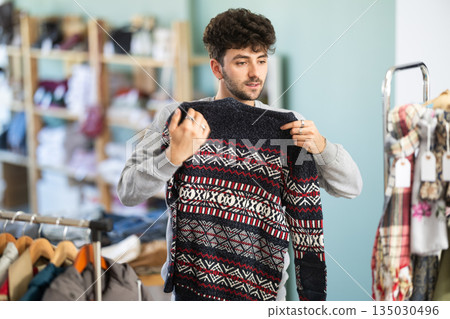 Young man chooses sweater in clothing store Young man chooses sweater in clothing store 135030496