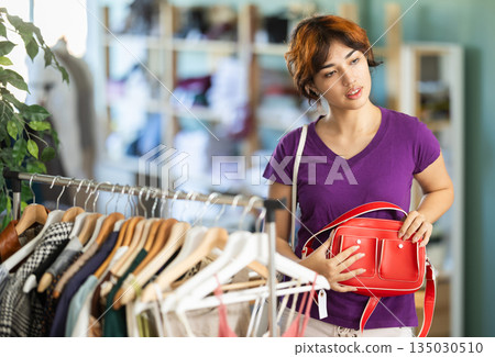 Curious girl looking at shoulder bag in clothing store Curious girl looking at shoulder bag in clothing store 135030510