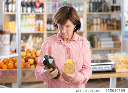 Mature woman choosing vegetable oil in grocery store Mature woman choosing vegetable oil in grocery store 135030569