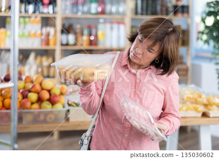 Female buyer carefully reads labels on packaging of semi-finished chicken or pork products - she chooses best product in supermarket Female buyer carefully reads labels on packaging of semi-finished chicken or pork products - she chooses best product in supermarket 135030602