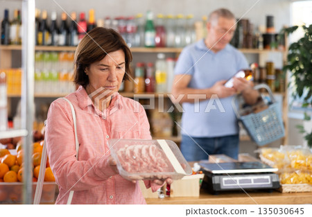 Woman chooses pork fillet, while her husband buys alcohol in supermarket 135030645