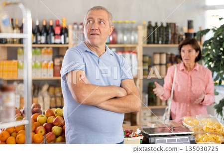 Senior wife stands behind pensioner husband and yells at companion. Senior wife stands behind pensioner husband and yells at companion. 135030725