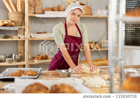 Young female apprentice baker kneading dough in bakery 135030728