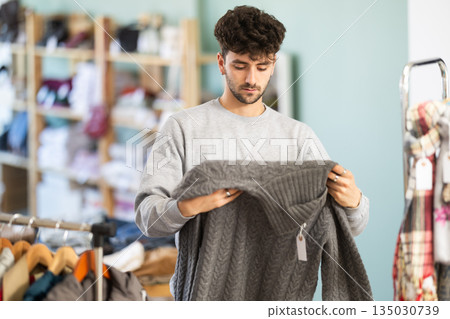Selective young guy choosing sweater in clothing store 135030739
