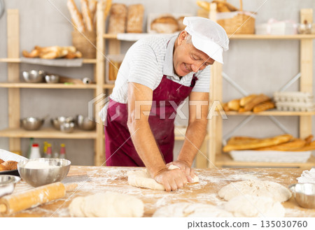 Elderly male baker kneading dough on table Elderly male baker kneading dough on table 135030760