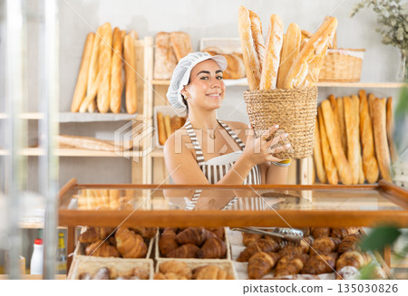 Young female seller with baguettes in basket 135030826