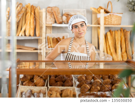 Young saleswoman puts croissants in plastic bag in bakery Young saleswoman puts croissants in plastic bag in bakery 135030850