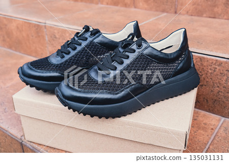 Elegant black leather womens shoes blank product for branding displayed on recycled cardboard box. New casual female sneakers no-brand footwear e-commerce. No logo product 135031131