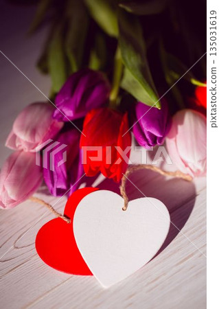 Colorful tulip bouquet is being shown in flat design on pale wooden surface with heart tags 135031619