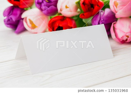 Flat design is showing blank tent-style card on wood tabletop with multicolor tulip bouquet behind Flat design is showing blank tent-style card on wood tabletop with multicolor tulip bouquet behind 135031968