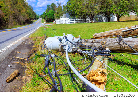 Fallen utility pole lies near rural road, with cables strewn on ground after bad tornado weather. 135032200