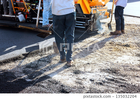 Workers prepare surface while machine lays fresh asphalt on road Workers prepare surface while machine lays fresh asphalt on road 135032204