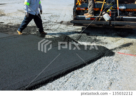 Workers operate paving machine spread asphalt during road construction in busy urban area. 135032212