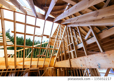 Construction site of house with exposed wooden beams roof framing under timber studs Construction site of house with exposed wooden beams roof framing under timber studs 135032217
