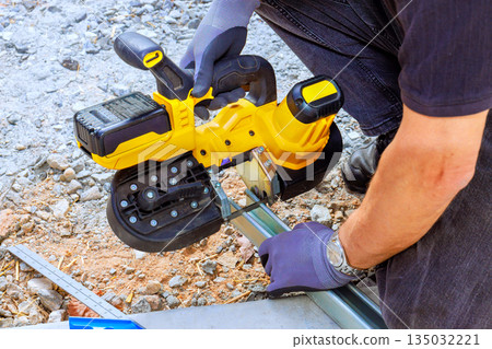 Worker operates cordless saw cutting tool on metal piping while on construction site Worker operates cordless saw cutting tool on metal piping while on construction site 135032221