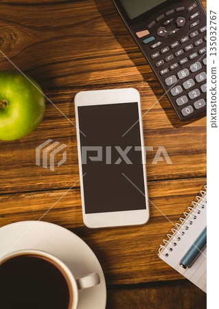 Showing desk with white smartphone alongside calculator, green apple, coffee, notebook and blue pen Showing desk with white smartphone alongside calculator, green apple, coffee, notebook and blue pen 135032767