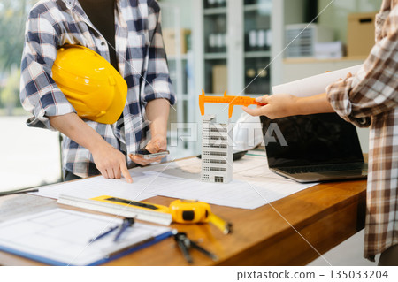 Two colleagues discussing data working and tablet, laptop with architectural project at construction site 135033204