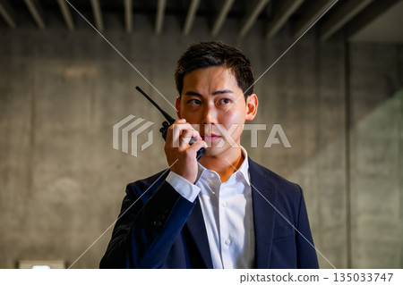Male security guard communicating via walkie-talkie Male security guard communicating via walkie-talkie 135033747