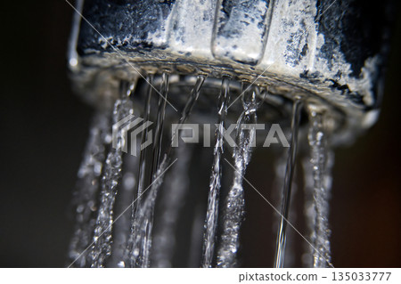 Close-up macro shot of water dripping from a faucet with mineral deposits 135033777