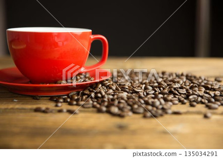 Flat design showing red coffee cup resting on wood table with scattered beans against dark backdrop 135034291