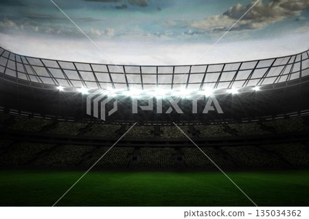 Empty stadium showing seating beneath metal roof, floodlighting green field under partly cloudy sky 135034362