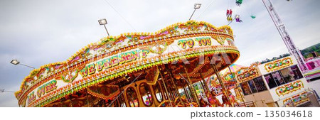 Flat design ornate carousel is standing on paved fairground with mounted horses multicolored bulbs 135034618